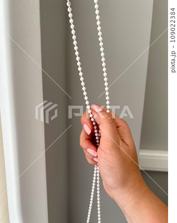 A female hand holding a beaded chain for the blinds. High quality photo A female hand holding a beaded chain for the blinds. High quality photo 109022384