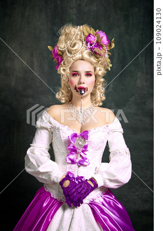 Sweet life. Young girl wearing in old fashion dress with corset licks the spoon she just ate chocolate against vintage background. 109024130