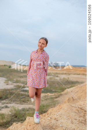 A teenage girl with long hair tied up in a ponytail in a short dress walks along a deserted canyon 109024566