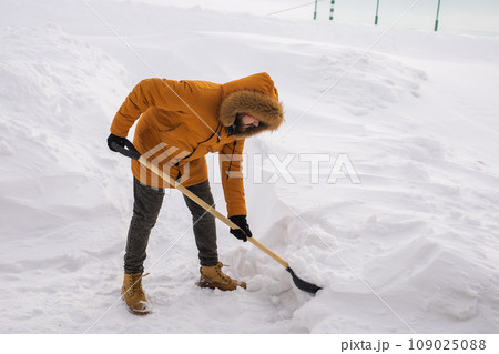 Man is clearing the snow near house and on staircases hovelling at the winter season. Winter storm and season specific Man is clearing the snow near house and on staircases hovelling at the winter season. Winter storm and season specific 109025088