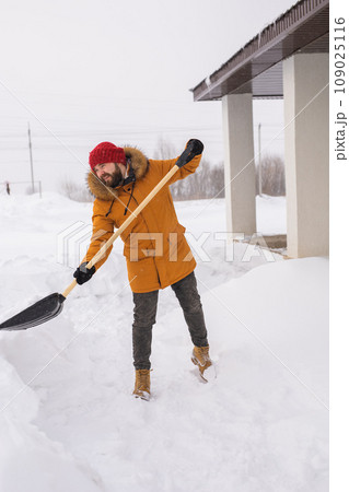 Young man clearing snow in his backyard village house with shovel. Remove snow from the sidewalk. 109025116