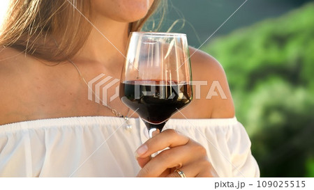 Closeup of woman stirring red wine in glass while standing on villa balcony or terrace 109025515