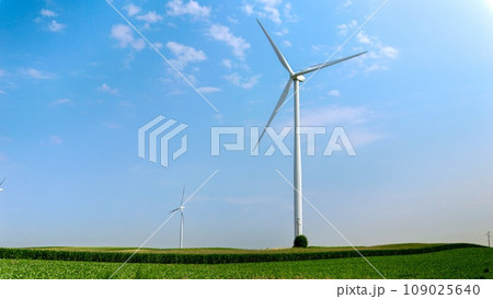 View on green fields and meadows with working wind powered turbines generating electric power View on green fields and meadows with working wind powered turbines generating electric power 109025640