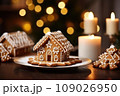 Gingerbread house on table. Defocused lights of Christmas garland. Evening in the living room. Holiday mood.  109026950