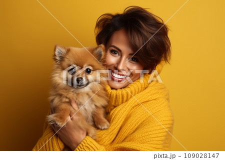 Young girl in yellow sweater with short brown hair holds a puppy and smiles on the yellow background 109028147