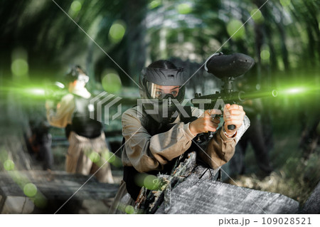 Paintball player in protective uniform aiming and shooting with guns Paintball player in protective uniform aiming and shooting with guns 109028521