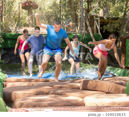 People trying to pass water obstacle course in adventure park People trying to pass water obstacle course in adventure park 109028635