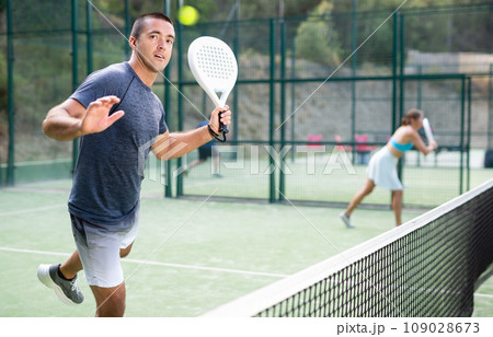 Man hitting ball with left-handed forehand while playing padel on open court Man hitting ball with left-handed forehand while playing padel on open court 109028673