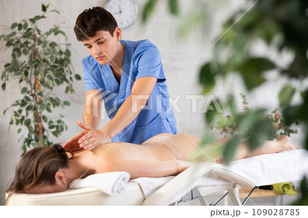 Young man carefully rubs neck area of young woman during general massage procedure. 109028785