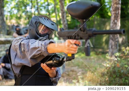 Woman in protective clothes and helmet aiming with paintball marker Woman in protective clothes and helmet aiming with paintball marker 109029155