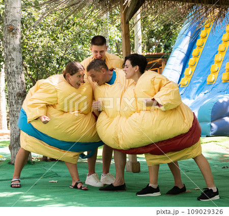 Two couples in inflatable double sumo suits fighting in outdoor playground 109029326
