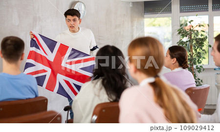 Young teacher holding flag of Great Britain in front of group of students 109029412