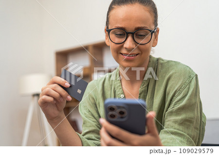 Simplified e-commerce: A delighted lady effortlessly processes her credit card payment on her phone for an online order. Simplified e-commerce: A delighted lady effortlessly processes her credit card payment on her phone for an online order. 109029579