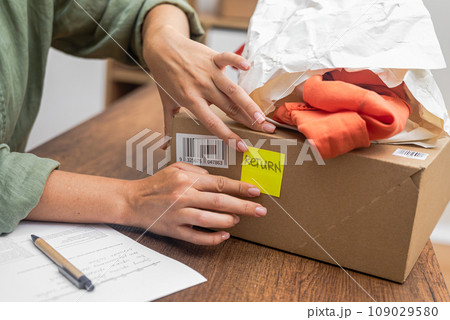 woman online shopper affixes a barcode sticker to a cardboard box, marking it for return and refund. woman online shopper affixes a barcode sticker to a cardboard box, marking it for return and refund. 109029580