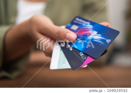In a close-up, a woman's hand clutches a stack of credit cards, highlighting online payments, shopping, and contactless credit card use. In a close-up, a woman's hand clutches a stack of credit cards, highlighting online payments, shopping, and contactless credit card use. 109029582