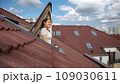 Happy smiling brunette woman opening attic window and breathing fresh air while looking on the cityscape with red tiled roofs 109030611