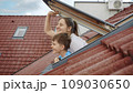 Happiness of a mother and her son as they open attic windows and peer outdoors, symbolizing the essence of family joy, parents with their children, and the excitement of a new home 109030650