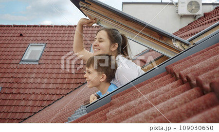 Happiness of a mother and her son as they open attic windows and peer outdoors, symbolizing the essence of family joy, parents with their children, and the excitement of a new home 109030650