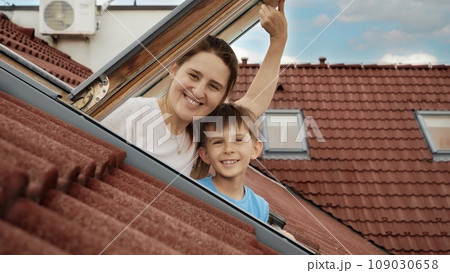 Delight of a mother and her son as they open attic windows and enjoy the view outside, illustrating the idea of family joy, parents sharing moments with their kids, and the excitement of relocating to 109030658