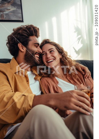 A young couple holding hands while sitting on a couch, watching a romantic comedy on TV 109031420