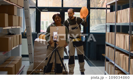 Warehouse marketing expert using smartphone placed on tripod to make ad campaign for social media platforms. African american influencer films herself in storage room showcasing her business 109034860
