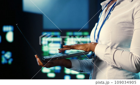 System administrator programming in server farm housing advanced equipment storing massive datasets. Programmer running code on laptop to mend data center racks doing complex computational operations 109034905