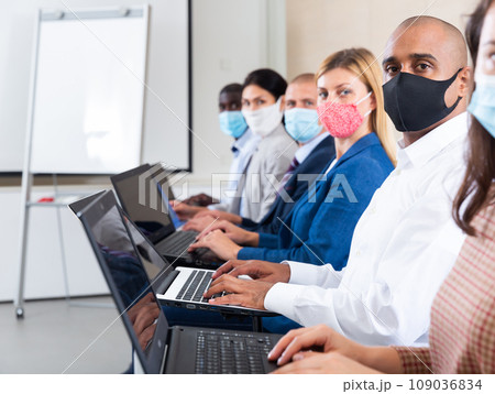 Side view of managers group in protective masks working at laptops in office Side view of managers group in protective masks working at laptops in office 109036834