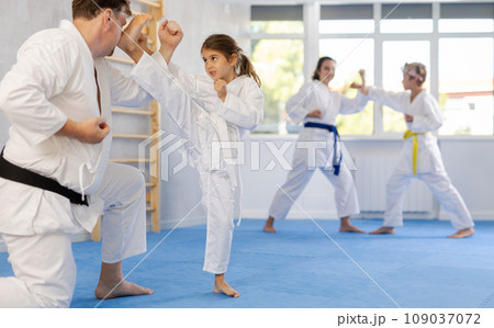 Preteen girl in kimono practicing karate kicks during sparring with father Preteen girl in kimono practicing karate kicks during sparring with father 109037072