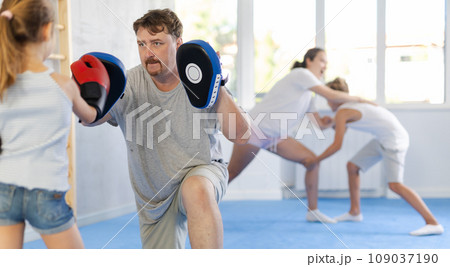 Man holding hitting pads during workout with tween daughter in boxing gloves 109037190