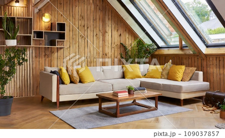 本棚のある木の壁にコーナーソファと素朴なテーブル、屋根裏部屋のモダンなリビングルーム。　AI生成画像 109037857