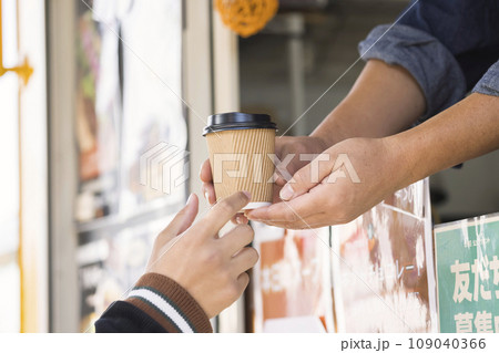 キッチンカーでコーヒーを購入し受け取る若い男性手元 109040366