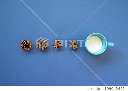 Cup of milk with pine cone on navy blue background. top view Cup of milk with pine cone on navy blue background. top view 109043445