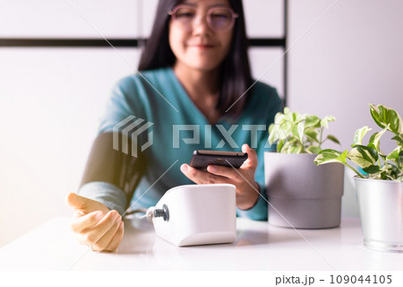 Asian woman holding mobile phone and using blood pressure monitor 109044105