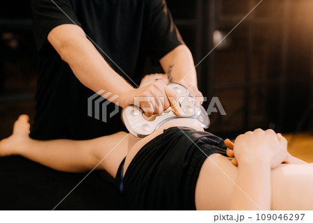 Therapist using IASTM instrument treatment, man receiving soft tissue treatment on her leg with guasha stainless steel tool, osteopathy 109046297