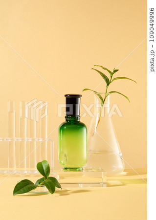 Minimal background with empty space for cosmetics, business branding and product presentation. A green bottle on glass podium with fresh tea leaves, flask and test tube rack on beige background Minimal background with empty space for cosmetics, business branding and product presentation. A green bottle on glass podium with fresh tea leaves, flask and test tube rack on beige background 109049996