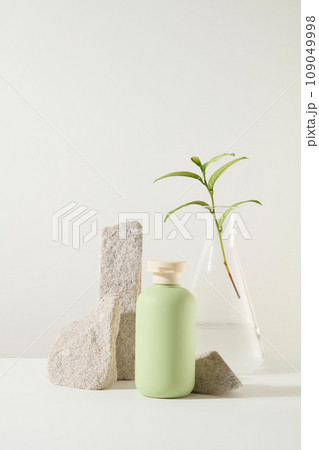 Minimal background for the presentation of products of green tea extract. Green beauty product bottle displayed on white background with gray blocks of stone and green tea leaves 109049998