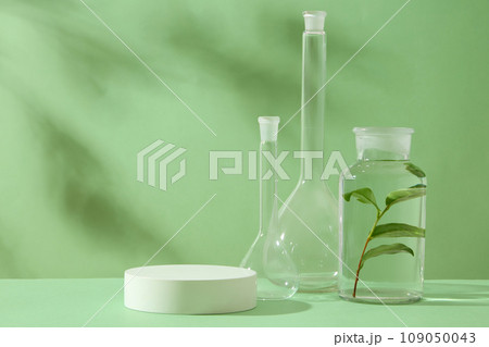 A round white podium placed on green background with glass flasks containing tea leaves. Scene for advertising and branding green tea extract and blank space for display product. Front view 109050043