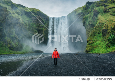 Powerful Skogafoss waterfall and male tourist walking in summer at Iceland 109050499
