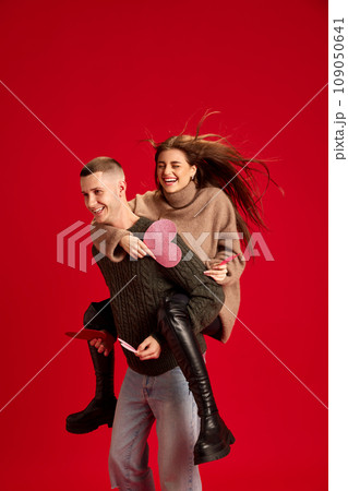 Playful, young, happy couple, man and woman, boyfriend and girlfriend having fun against red studio background. Valentine's day, relationship Playful, young, happy couple, man and woman, boyfriend and girlfriend having fun against red studio background. Valentine's day, relationship 109050641