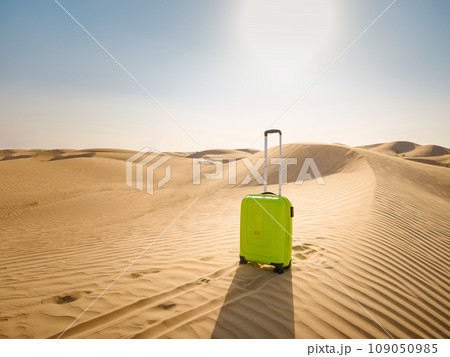 bright light green or yellow suitcase in sands of desert dunes. Concept and idea of travel to United Arab Emirates, Dubai sands at sunset. Summer holiday travel concept 109050985