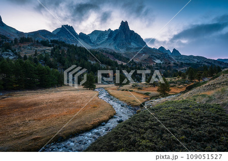 Sunset over Claree Valley with Main De Crepin peak and river flow through in larch forest during autumn at French Alps, France Sunset over Claree Valley with Main De Crepin peak and river flow through in larch forest during autumn at French Alps, France 109051527