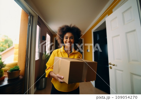 Close-up portrait of female delivery courier with cardboard box at client's door. Confident positive African American young woman delivering parcel to a client. Logistic and delivery concept. Close-up portrait of female delivery courier with cardboard box at client's door. Confident positive African American young woman delivering parcel to a client. Logistic and delivery concept. 109054270