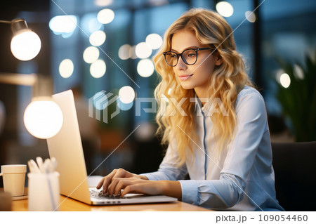 Portrait of a beautiful young Caucasian woman using a laptop in a modern bright office. Concentrated serious business woman working late into the night to complete a successful business project. 109054460