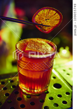 Glass with delicious cocktail, decorated with dry slice of orange. Neon colored bar. Bartender profession 109055749