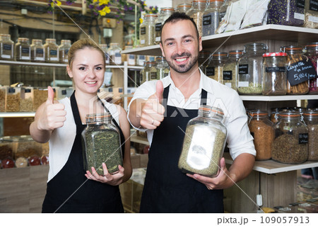 Man and woman sellers posing with banks of dried herbs in store Man and woman sellers posing with banks of dried herbs in store 109057913