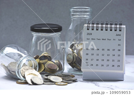 June 2024 calendar and glass jars with multicurrency coins. June 2024 calendar and glass jars with multicurrency coins. 109059053