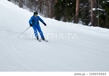 A man in blue sportswear on skis rides down a snowy slope 109059984