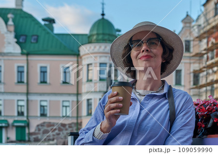 A girl drinks coffee from a paper cup in a coffee shop on the street of an ancient city A girl drinks coffee from a paper cup in a coffee shop on the street of an ancient city 109059990