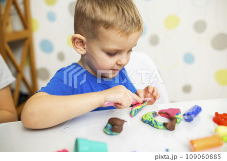 Little boy enthusiastically plays with plasticine, play dough on white table Little boy enthusiastically plays with plasticine, play dough on white table 109060885