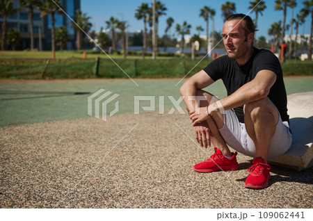 Handsome Caucasian sportsman relaxing after heavy workout in the outdoor urban sportsground. People and sport concept Handsome Caucasian sportsman relaxing after heavy workout in the outdoor urban sportsground. People and sport concept 109062441